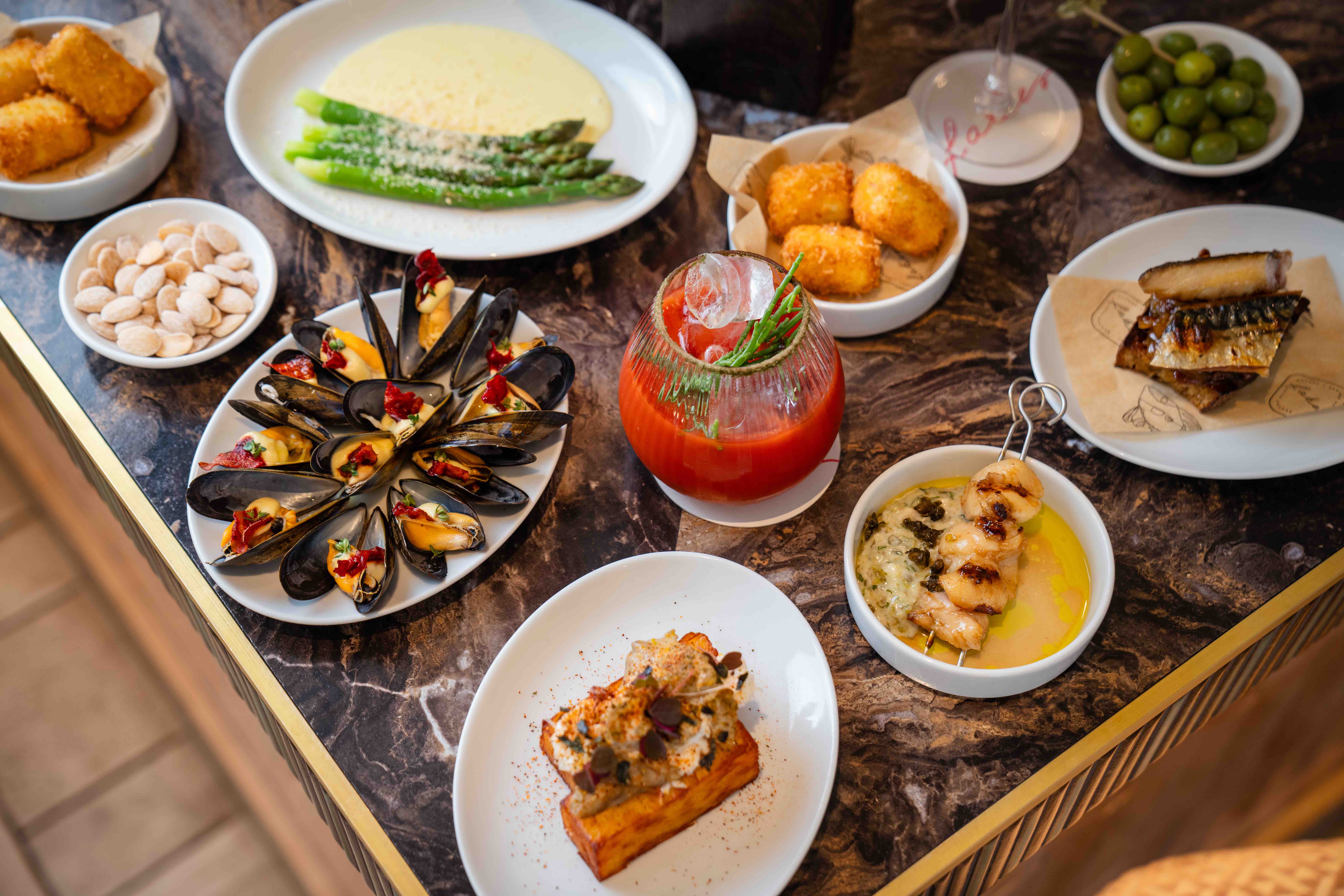 A selection of small plates on the marble trim bar at Faber, crab on a square potato terrine, croquettes, dressed mussels, a bloody mary in goblet in centre of picture, mackerel and asparagus in