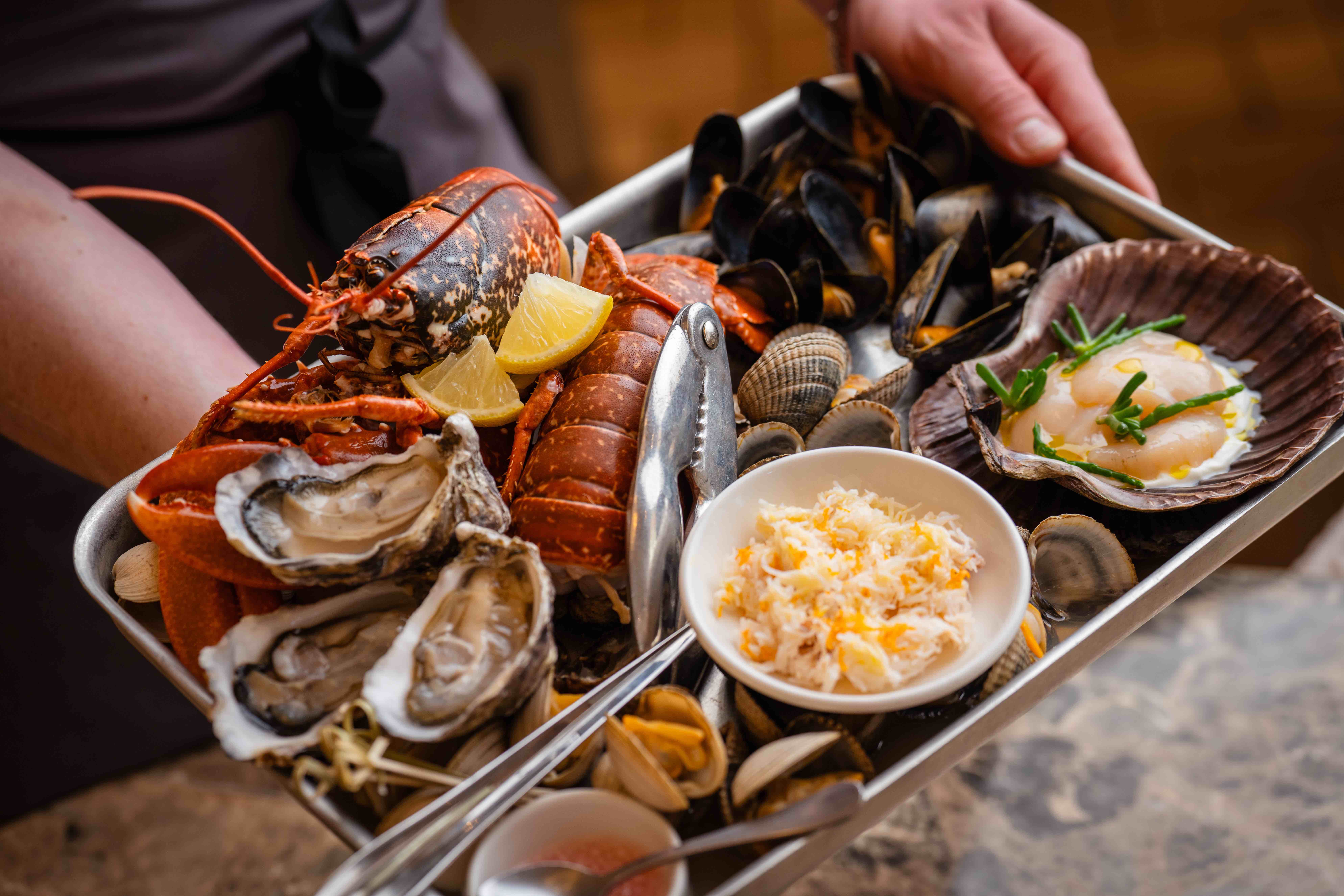 Selection of shellfish including lobster, oysters, clams, whales & mussels. on a nickel tray and held by a smartly dressed team member.