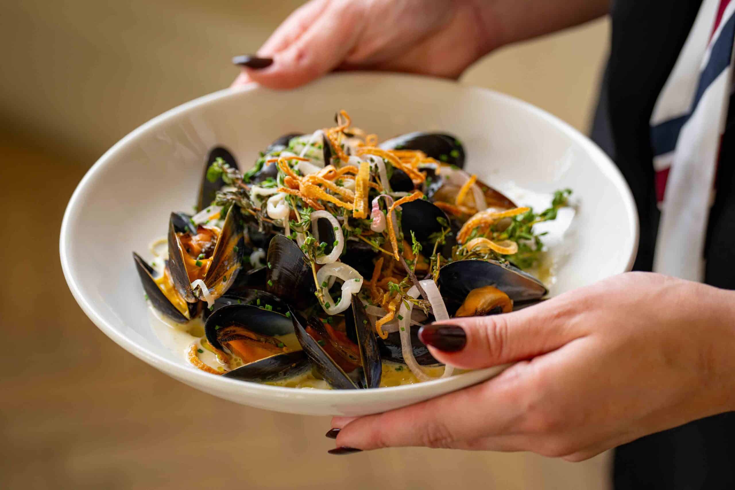 A woman holding a dish of mussels and vegetables