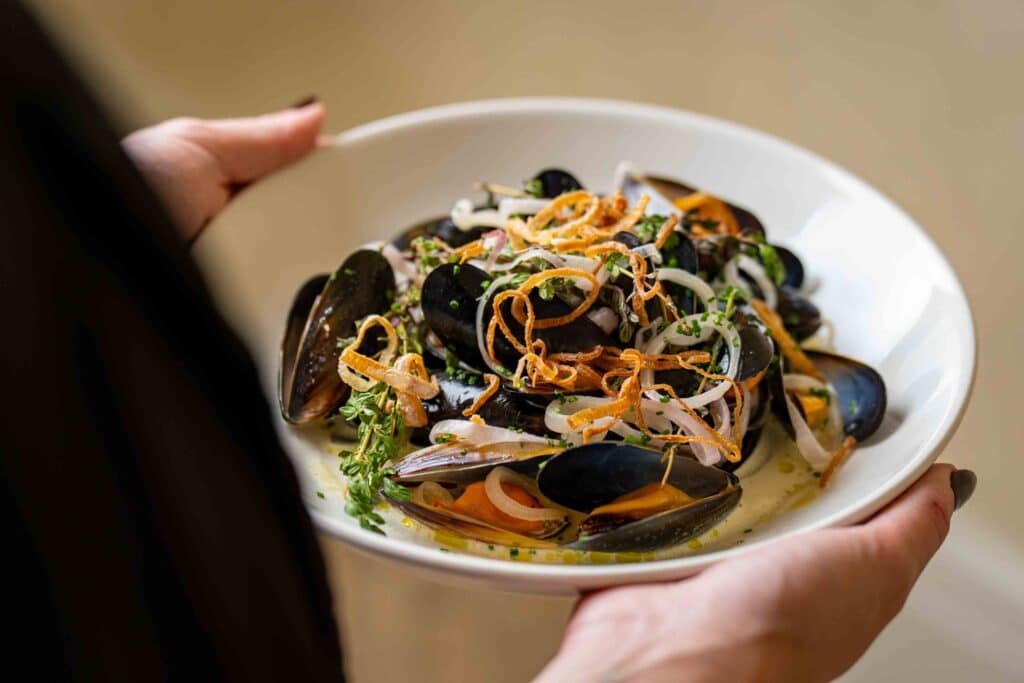 A woman holding a dish of mussels and vegetables