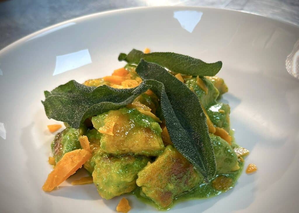 Butternut squash gnocchi prepared and on white plate with green pesto and dried sage leaf garnish and rich orange pumpkin colours