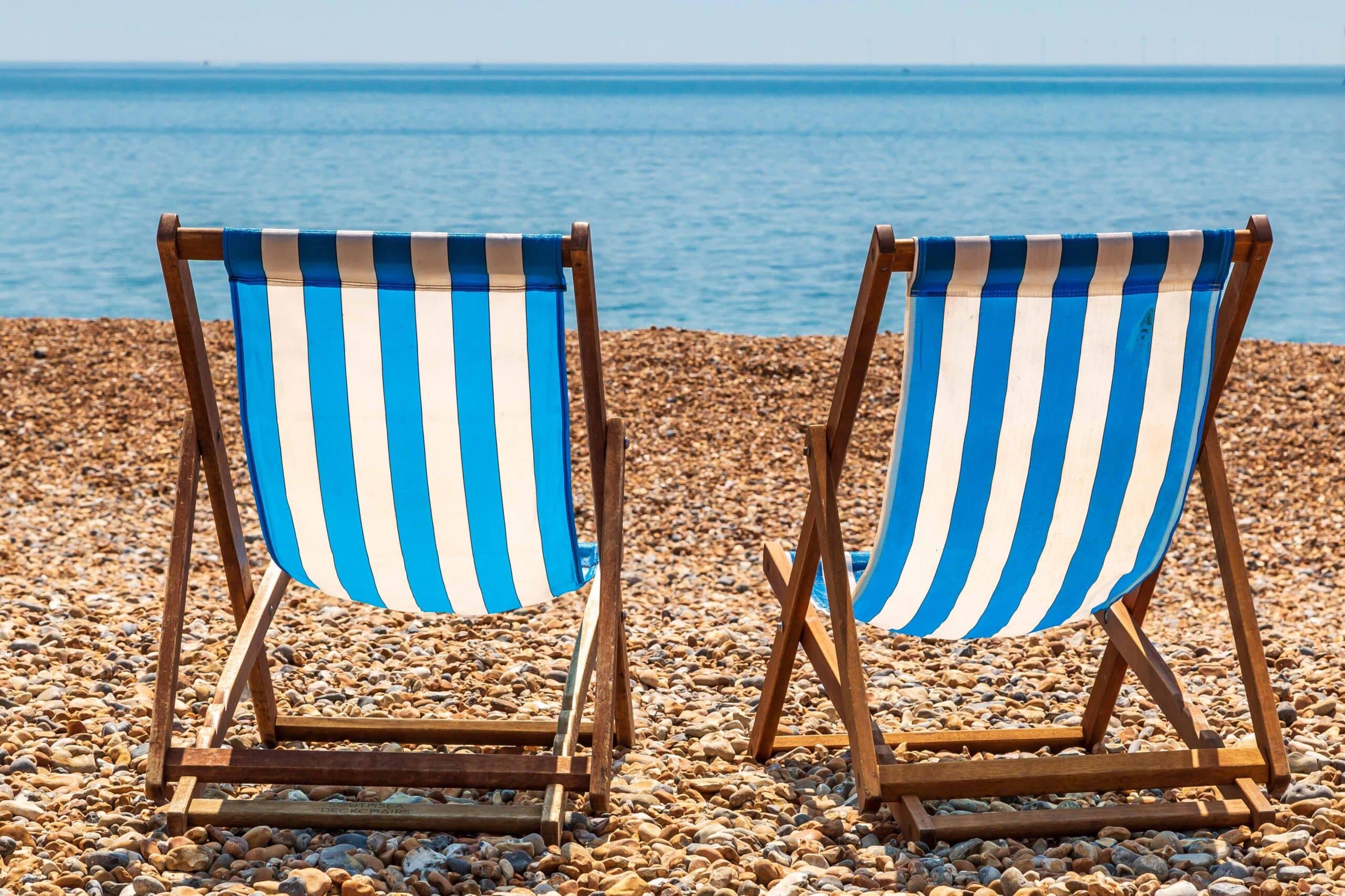 Two empty wooden deck chairs, blue and white striped fabric, on brighton Beach, on a sunny summer's day