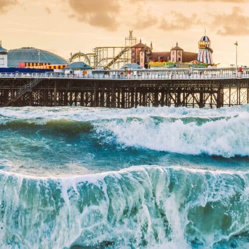 Brighton Pier, Brighton, Sussex, Britain on a stormy evening at dusk as the sun is setting. There are high waves and surf on the beach