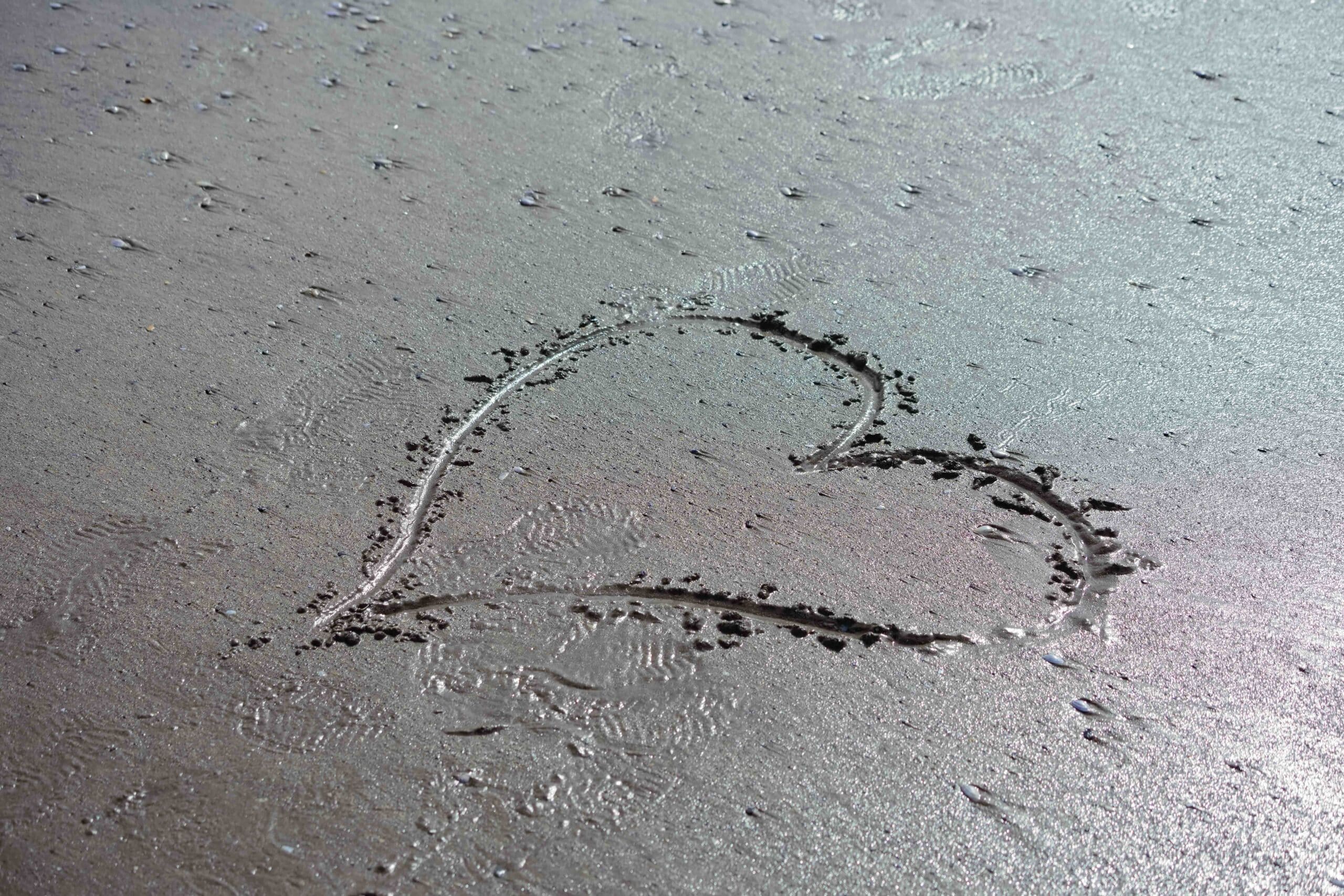 Heart drawn in the wet sand at Broad Haven beach in Pembrokeshire reflecting sun of wet sand