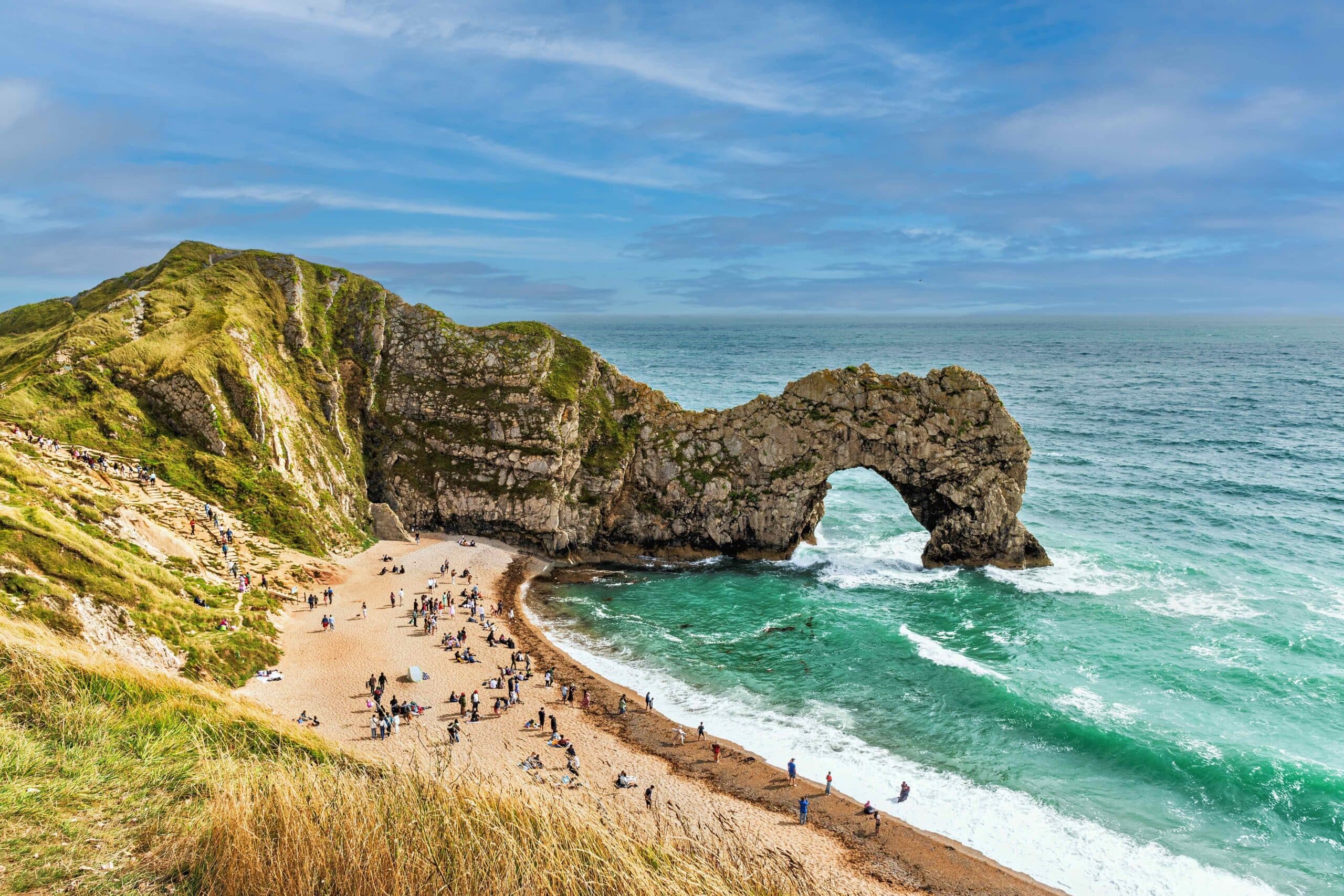 Durdle Door landmark, British cliffs on jurassic coast, deep blue sea, steep cliff with arch over sea and coastal slope with grass to the left.