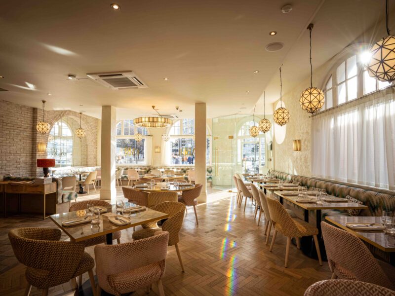 Faber restaurant with bright sunlight beaming through the large arched windows, casting light across the airy interior and coastal inspired furniture.