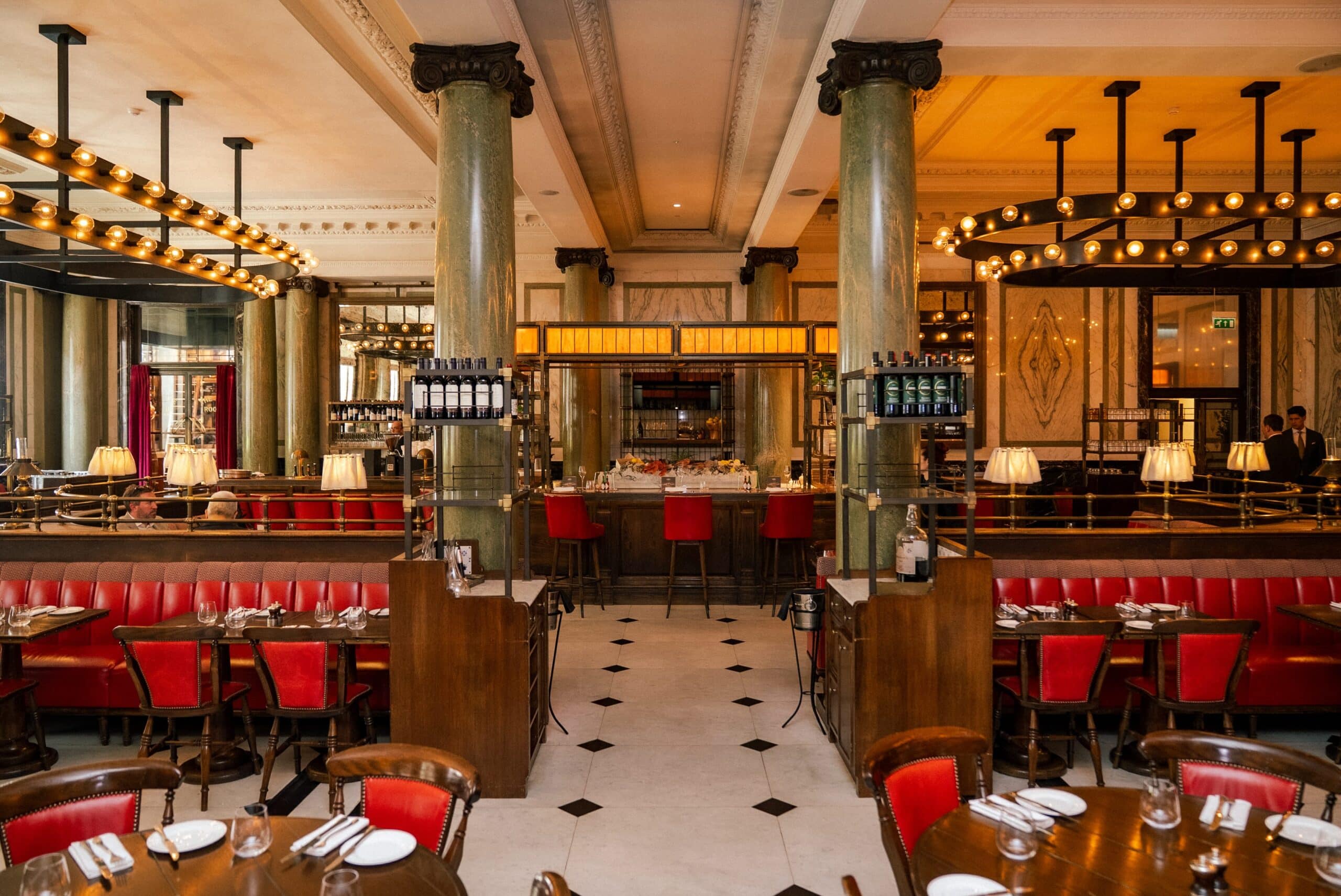 The grand dining room at The Rosewood Hotel in Holborn. Red leather seats, black and white tiled floor, spectacular warm lighting, marble columns and our fish counter front and centre.