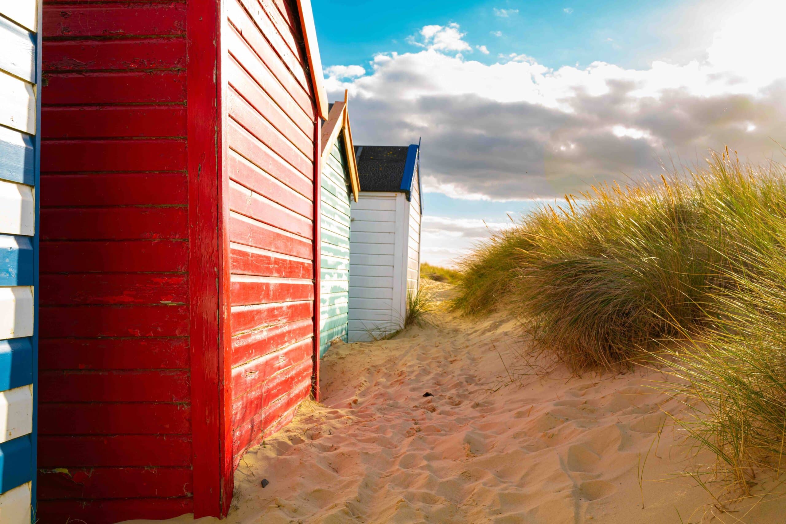 ow of brightly painted beach houses seen on golden sand by sand dunes. Located on the Suffolk coast in the UK.