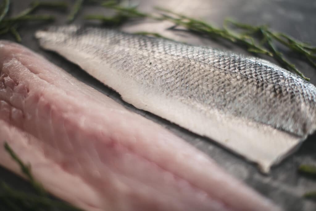 Filleted fish with silver scales on a nickel service surrounded by a bed of samphire