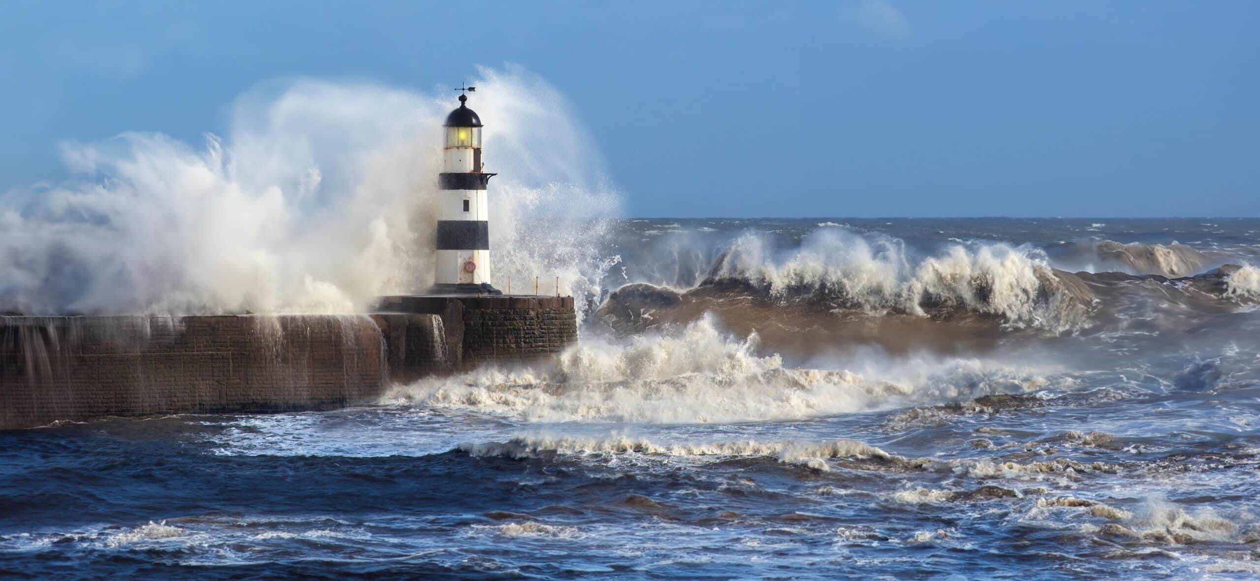 Waves crashing over Seaham Lighthouse on the northeast coast of England.Concrete stone harbour with wave crashing over below the lighthouse. UK winter storm.