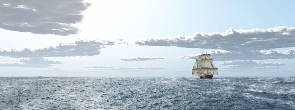 tall sailing ship with massive sails on blue rippled ocean and blue skies with one line of cloud in the background