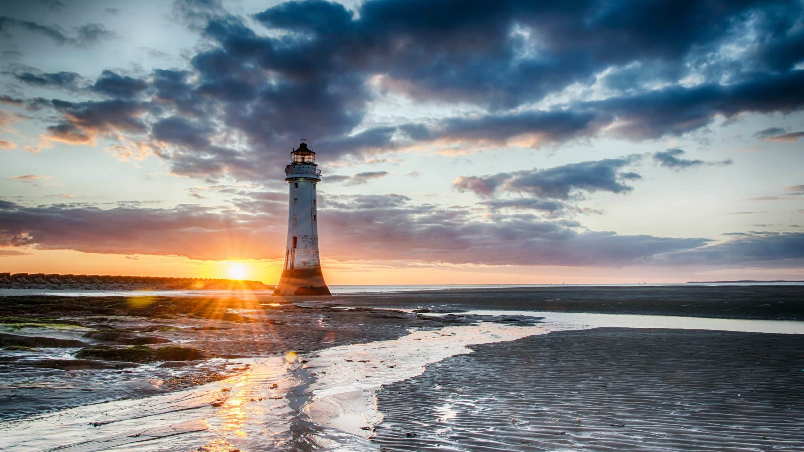 Lighthouse on rocks with sunset in background with epic orange and purple sky. tidal stream running through foreground