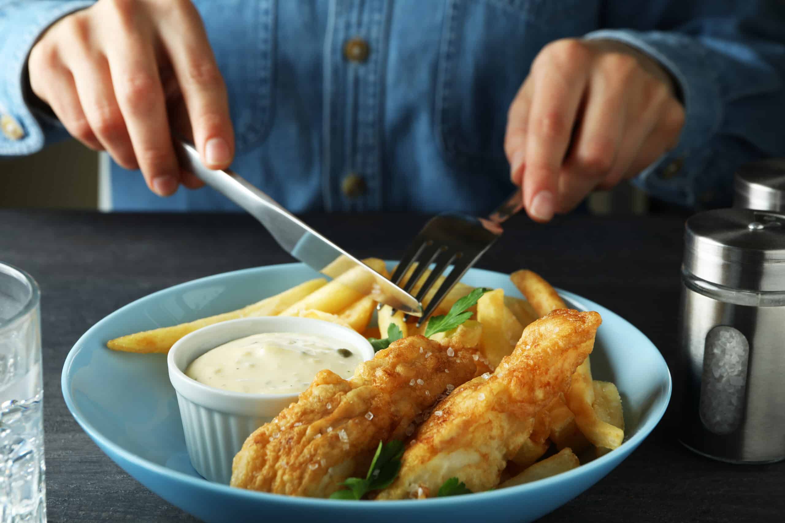 Woman eating fried fish and chips on dark table, close up